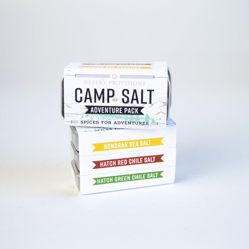 small aluminum container wrapped in a paper label. the label reads " Camp Salt adventure pack. spices for adventures. sonoran sea salt, hatch red chile salt, and hatch green chile salt"