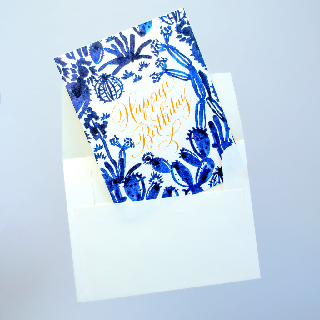 white card with various blue succulents and "happy birthday" written in gold at the center
