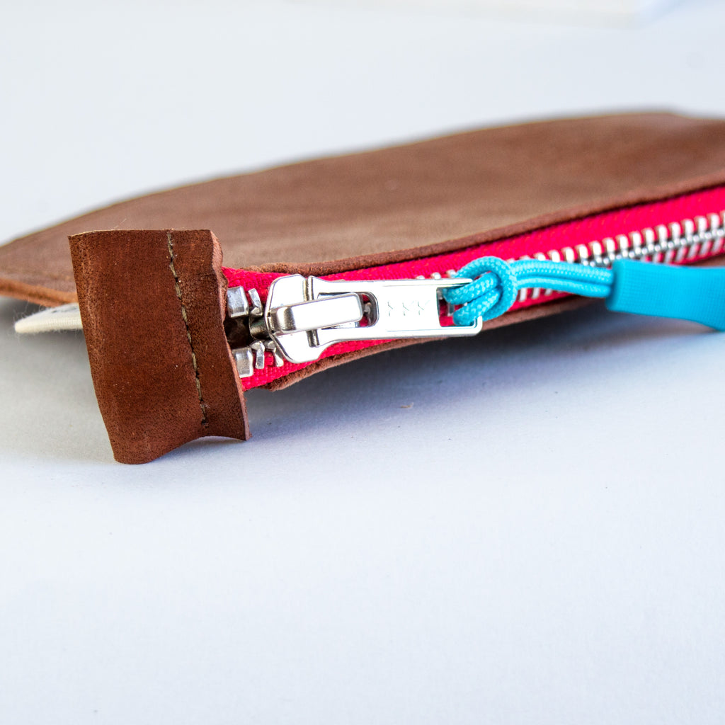 Small brown leather pouch with red zipper and blue zipper pull.