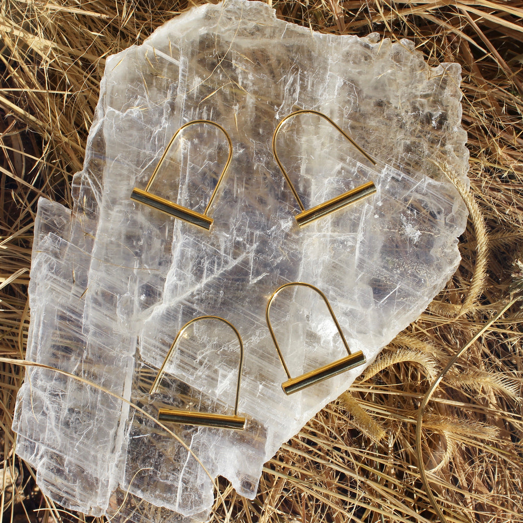 Two sets of golden earrings resembling bike locks atop a large quartz slab. One of each of the pairs of earrings is unfastened as an example of how to put them on.