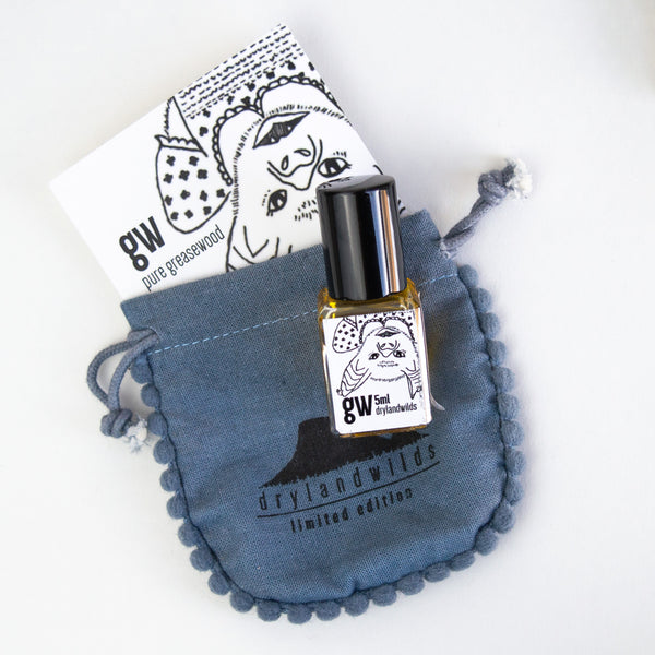 Small glass rollerball bottle with a black lid. the bottle contains a greasewood perfume oil. the oil has a blue linen bag to be stored in.