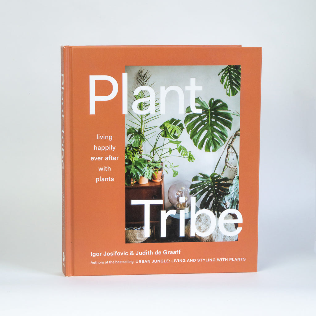 A cover of the book "Plant Tribe" by Igor Josifovic & Judith de Graaff. The cover is orange with a photo of lots of plants in a room next to a sheepskin rug. Additional text reads "Living Happily Ever After with Plants."