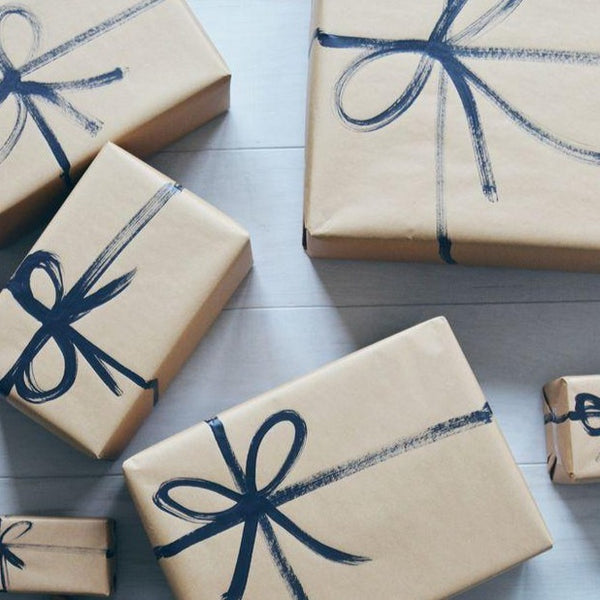 Multiple boxes wrapped in a tan wrapping paper with a blue bow hand painted on each