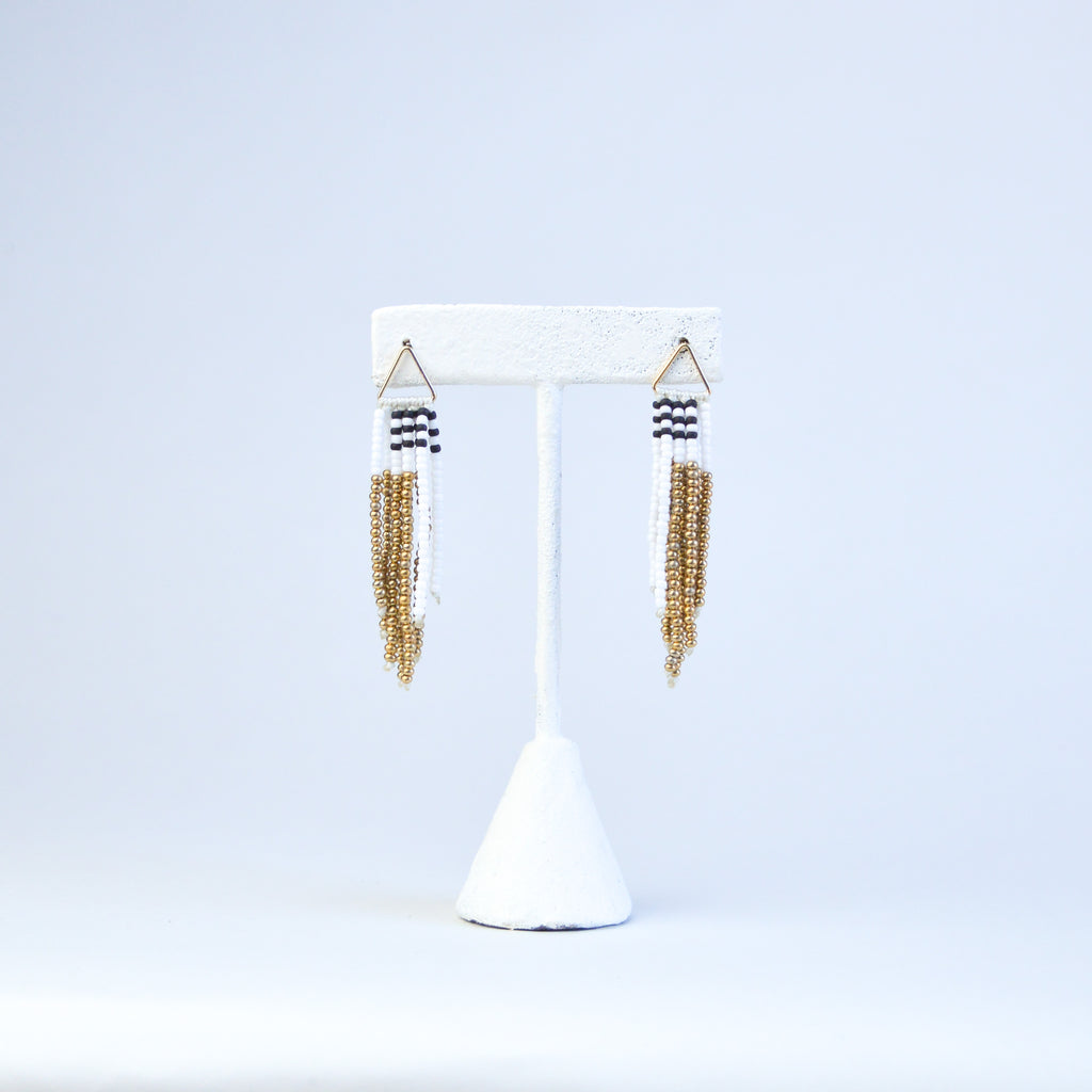 Pair of tassel earrings with asymmetric beading of gold, white and brown beads. The earrings are connected to the gold finding with a golden triangular loop.