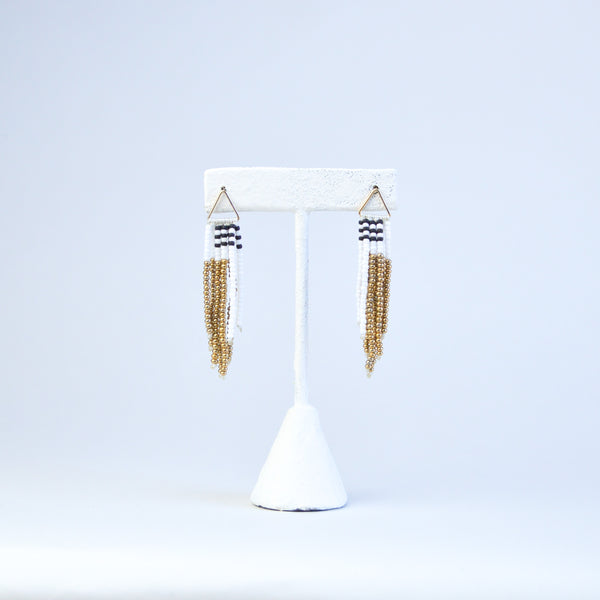 Pair of tassel earrings with asymmetric beading of gold, white and brown beads. The earrings are connected to the gold finding with a golden triangular loop.