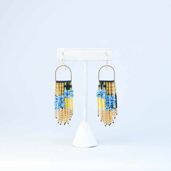 beaded fringe earrings with gold, white, black, yellow, green, and turquoise beads in an asymmetric pattern. the beads are connected to the finding by a golden semicircle.