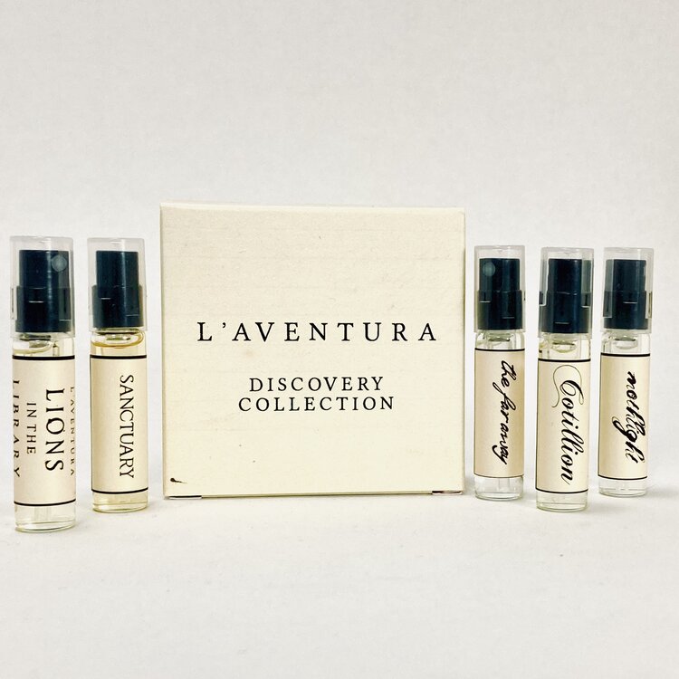 Five small perfume bottles next to an equally small cardboard box. The box has black text reading "L'aventura Discovery Collection."