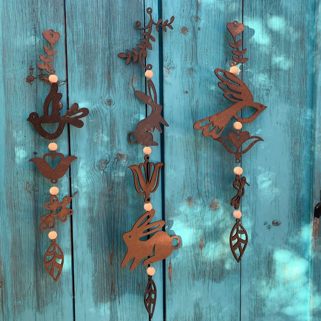 Three long wooden mobiles, from left to right: dove and hummingbird, rabbit, and swallow. The wooden animals are separated by wooden leaves, flowers, and circular beads.