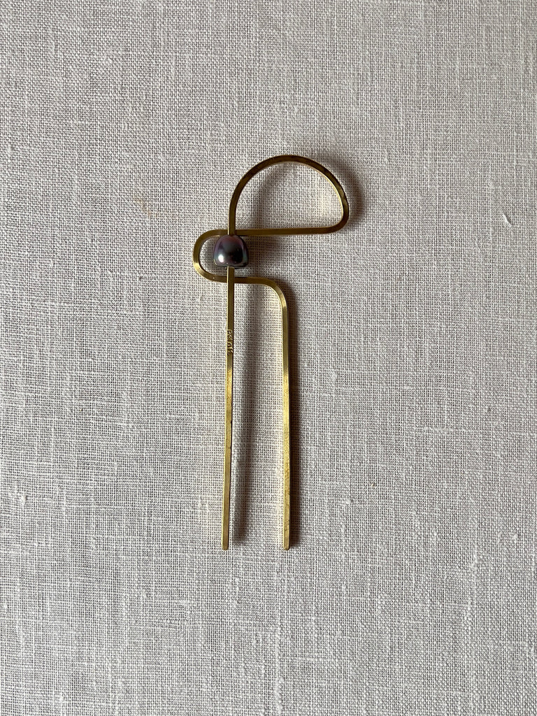 Curvy brass hair fork with a half circle at the top and to the side and a navy blue bead in the middle