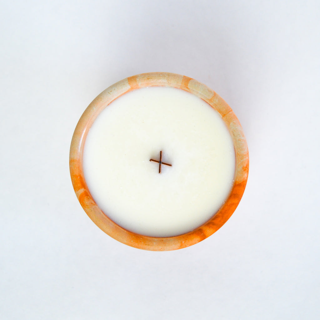 Top down view of a candle with a marbled orange vessel, showcasing the candle's white wax and wooden wick.