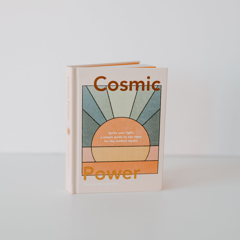 Book with a white base color. On top of the white base is a sun with the colors blue, orange, pink and yellow in a stained glass style. There is text on the top and bottom of the book cover reading "cosmic power."