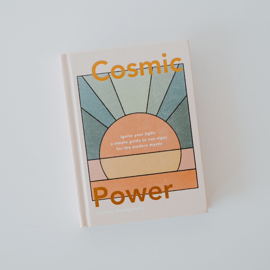 Book with a white base color. On top of the white base is a sun with the colors blue, orange, pink and yellow in a stained glass style. There is text on the top and bottom of the book cover reading "cosmic power."
