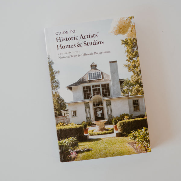 Cover of the book "Guide to historic artists' homes & studios" by Valerie A. Balint in collaboration with the National Trust for Historic Preservation. The cover is a photoraph of a historic house surrounded by grass, trees and bushes.