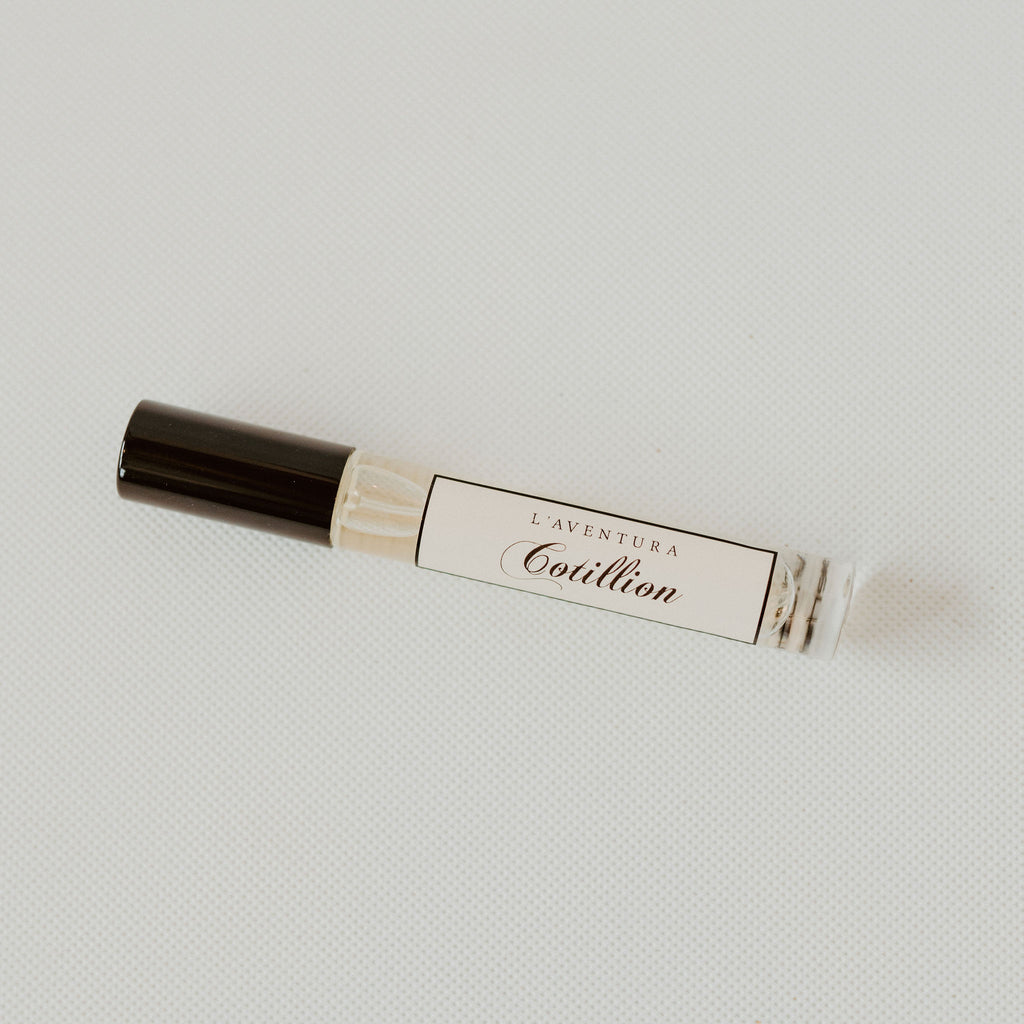 Small glass tube of perfume with a black lid.  The tube has a white label with black text reading  "l'aventura cotillion"