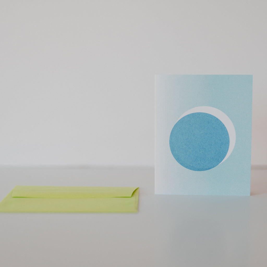 A card with a lunar eclipse on it, sitting next to an evelope on a white backdrop.