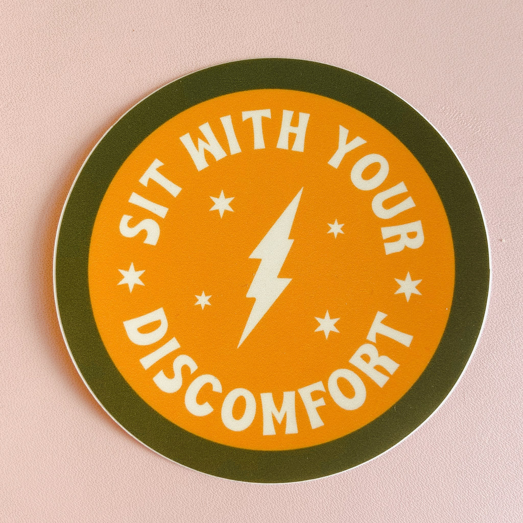 Circular sticker with a green boarder and yellow middle. theres a white thunderbolt in the middle and white lettering around it reading "sit with your discomfort."