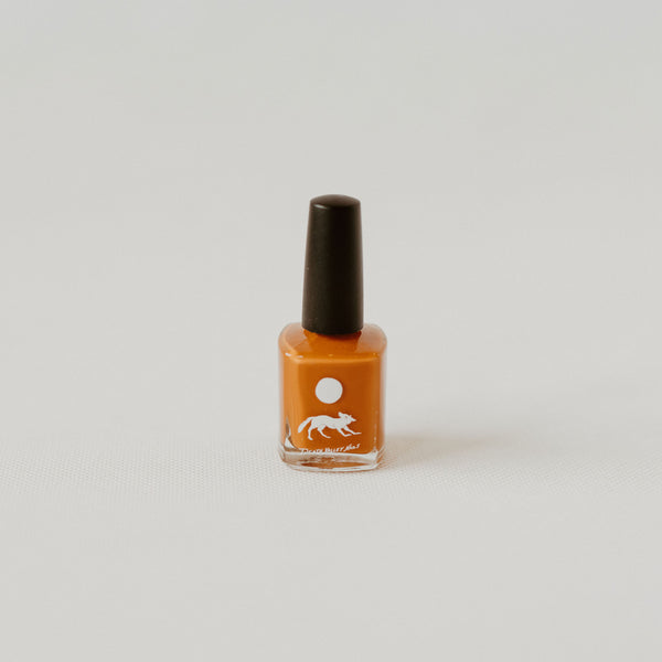 Orange nail polish in a clear bottle with a black lid. Theres a white label with a coyote under the moon and text reading "death valley nails."