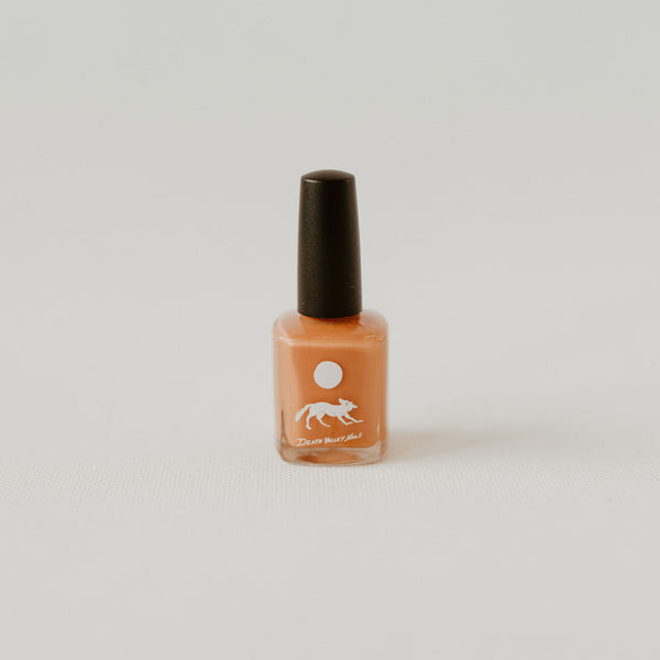 Light orange nail polish in a glass bottle with a black lid. There is a white label depicting a coyote under a full moon. there is text under the coyote reading "Death Valley Nails."