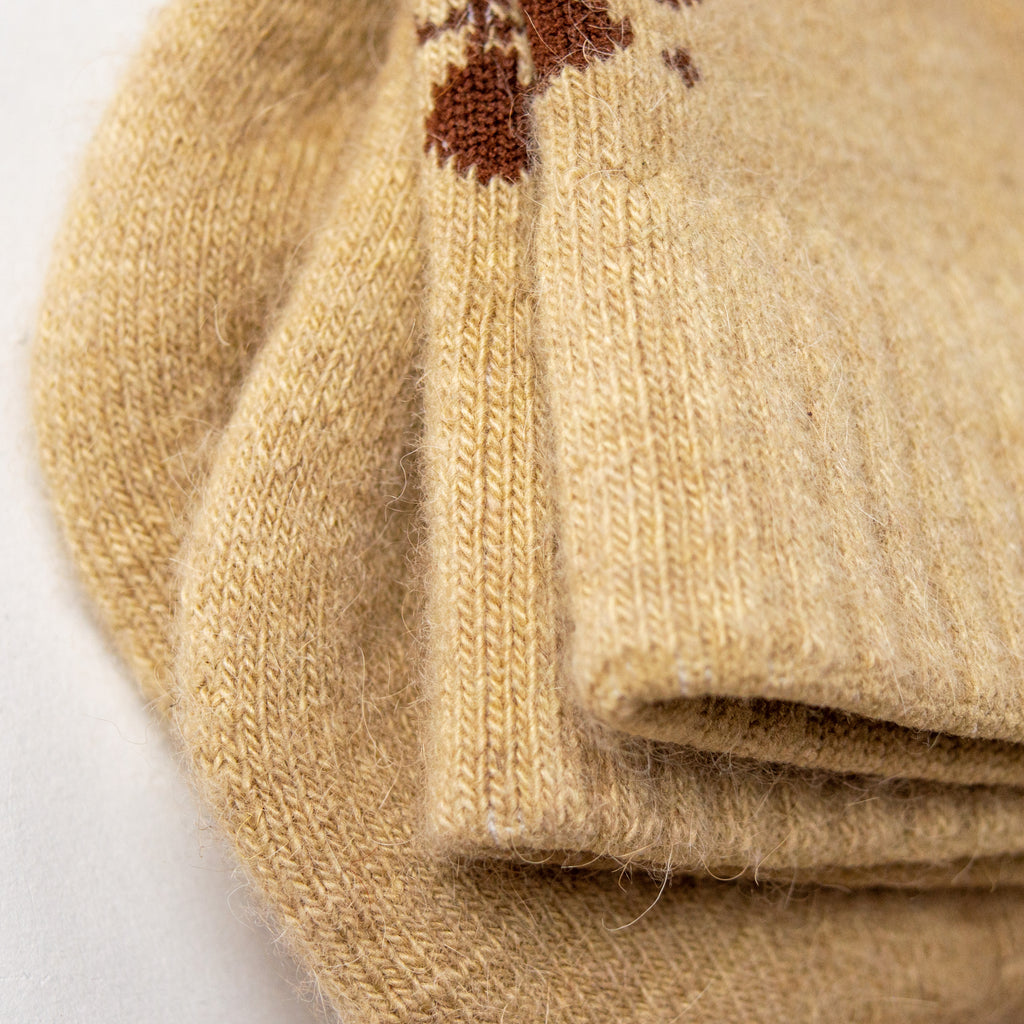 Closeup light tan socks on top of one another. The cuffs of the socks are ribbed and there are dark brown geometric shapes woven in at the back.