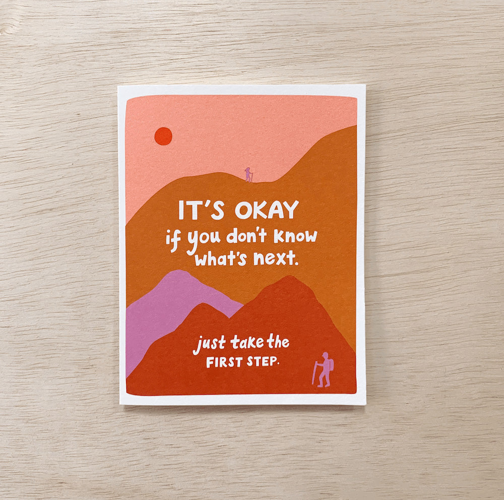 A card that has a mountain scene printed on it with the sun and hikers. It says: It's okay if you don't know what's next. Just take the first step.