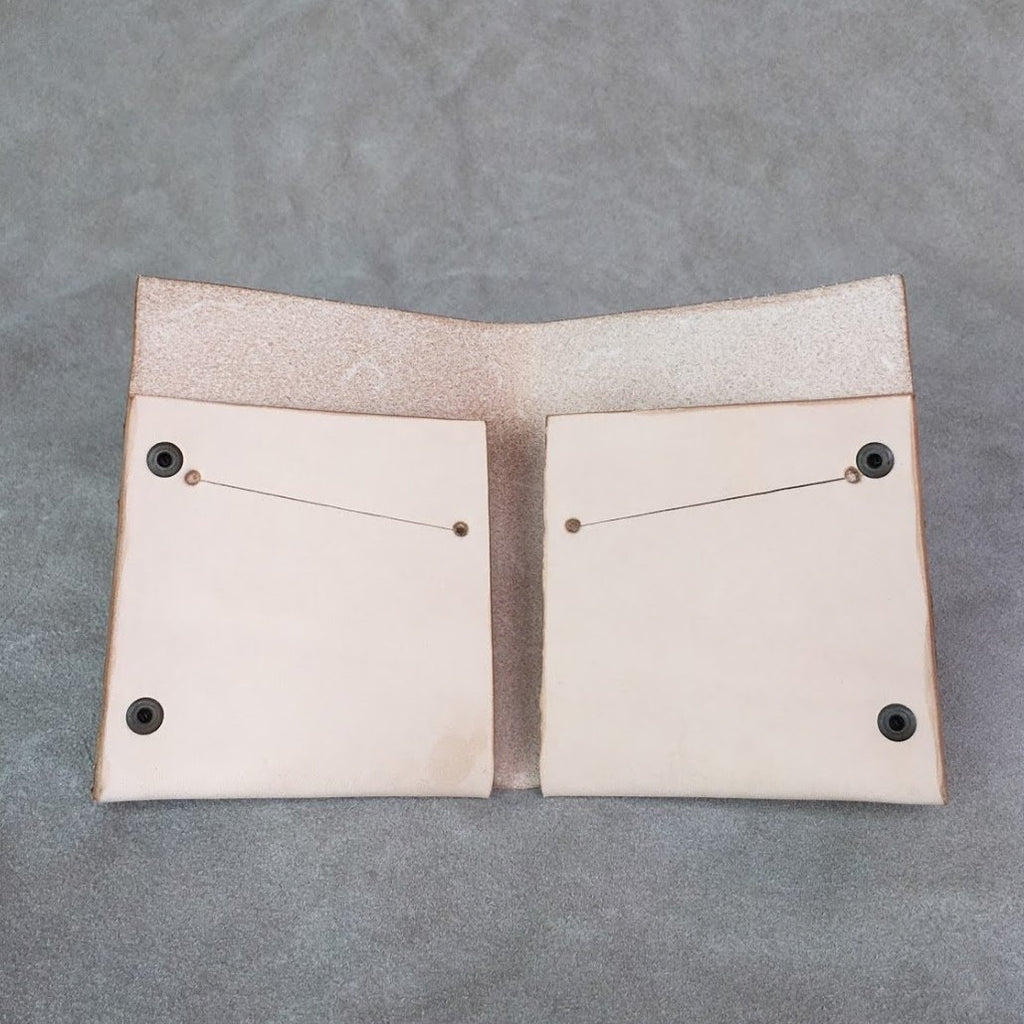 Photo of a tan wallet with black grommets. The wallet is open and laying on its back to showcase its 4 card or cash slots.