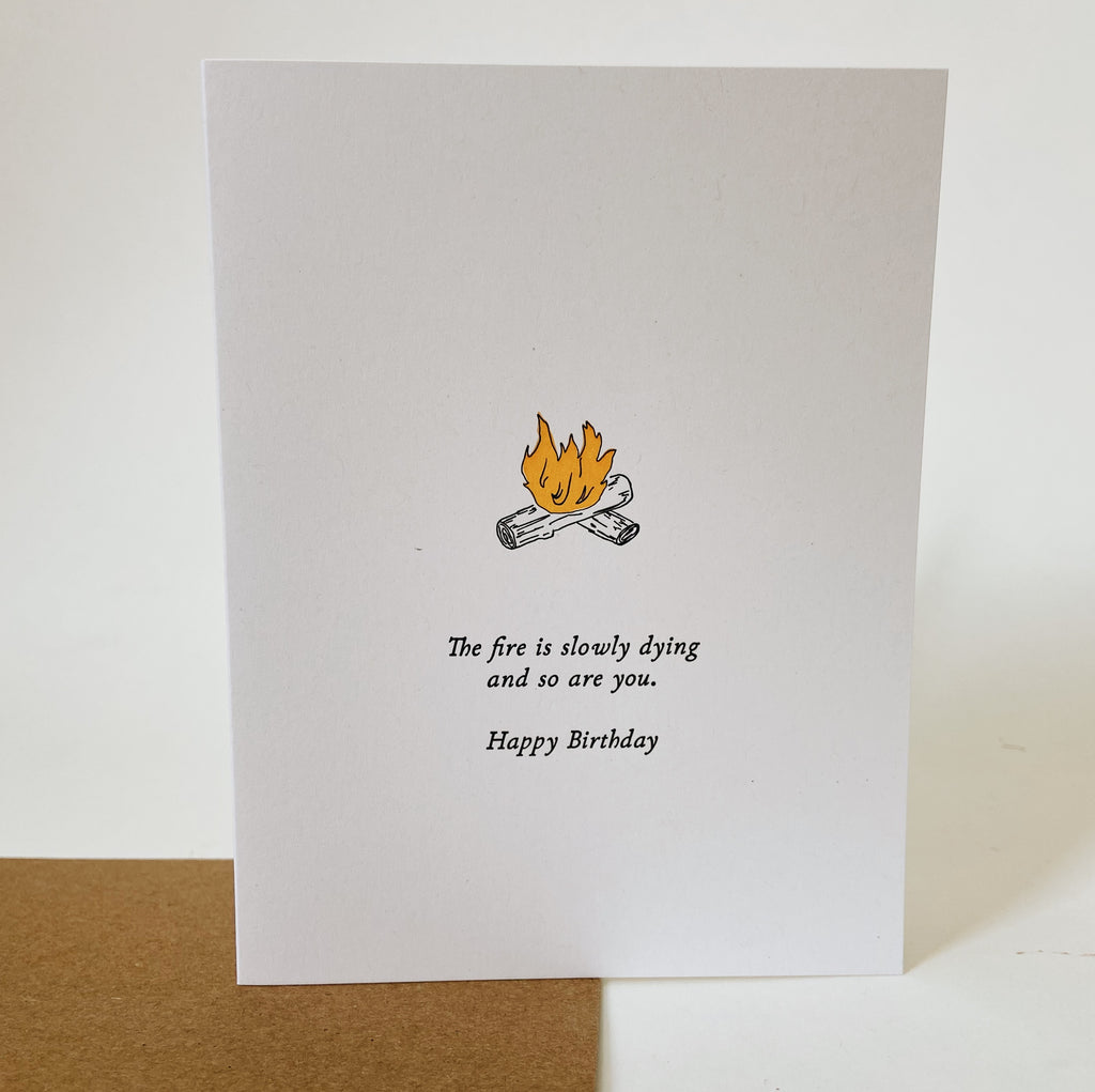 white card with a campfire. the logs are white with black outlines and the fire is orange. there is black text under it reading "the fire is slowly dying and so are you. happy birthday." 