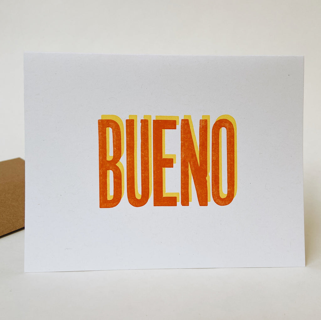 A white card with red and yellow text reading "Bueno." The yellow text is behind the red text to create a 3d effect.