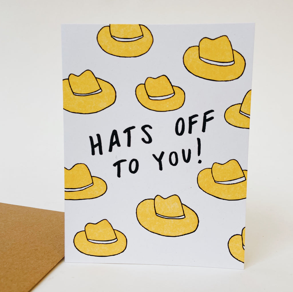 Multiple tan doodle styled hats randomly repeated on a white card. The middle of the card has white lettering reading "Hats off to you!"