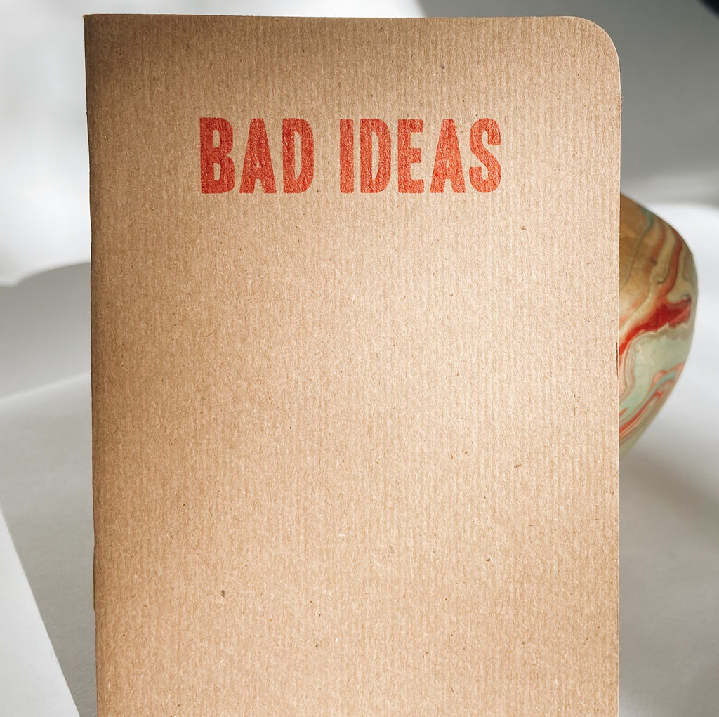 A tan paper notebook with red lettering at the top reading "Bad Ideas."