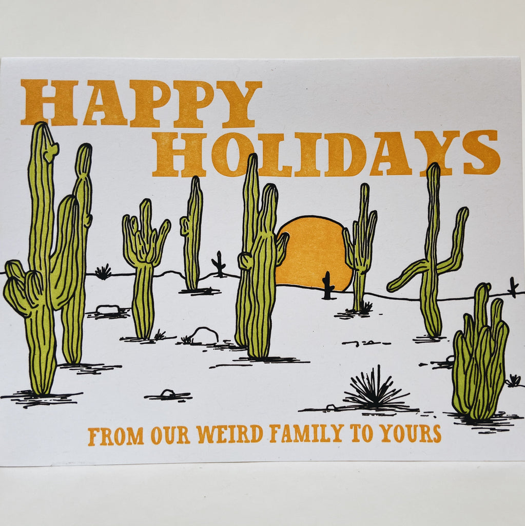 White card with multiple saguaro cacti with yellow text on the top and bottom reading "Happy Holidays from our weird family to yours."