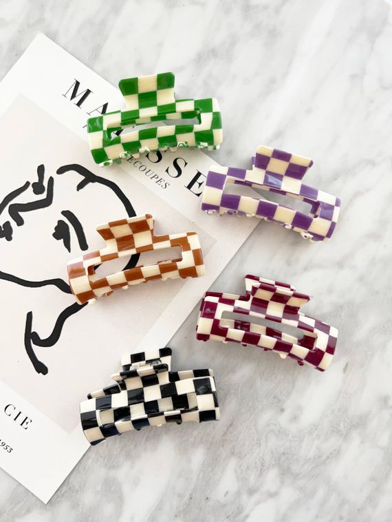 Five checkered hair claws of different colors. From top to bottom: green and white, purple and white, light brown and white, maroon and white, and black and white.