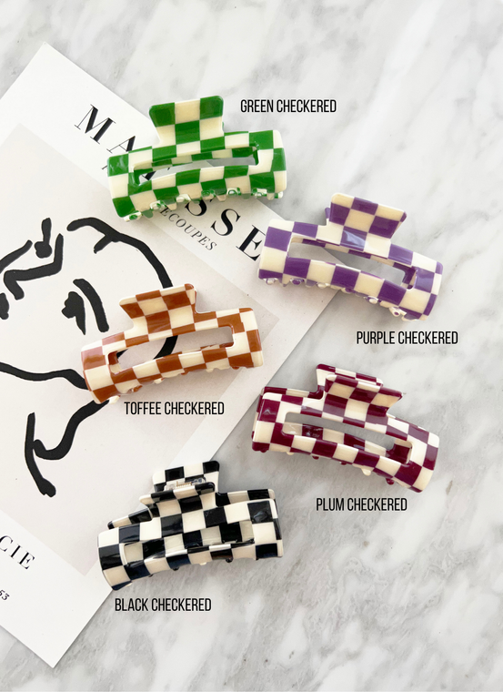 Five checkered hair claws of different colors. From top to bottom: green and white, purple and white, light brown and white, maroon and white, and black and white.