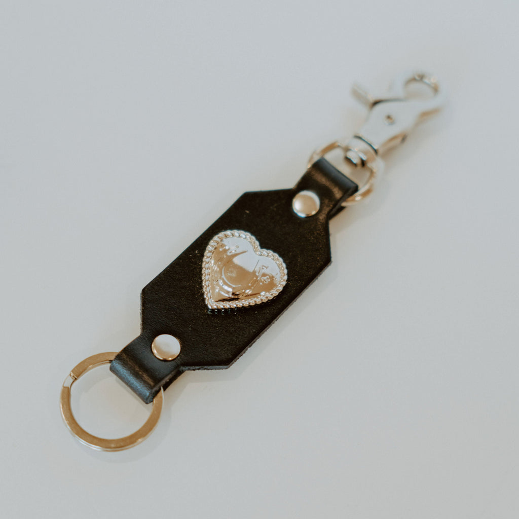 Black leather keychain with a key ring on one side and a silver hook on the other. there is a silver heart in the middle.