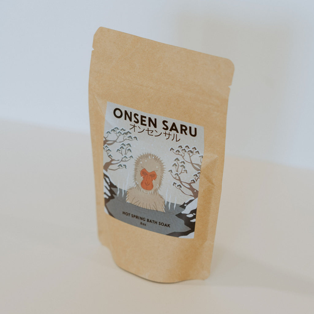 Brown paper bag with a blue label and black text reading "Onsen Saru hot spring bath soak."