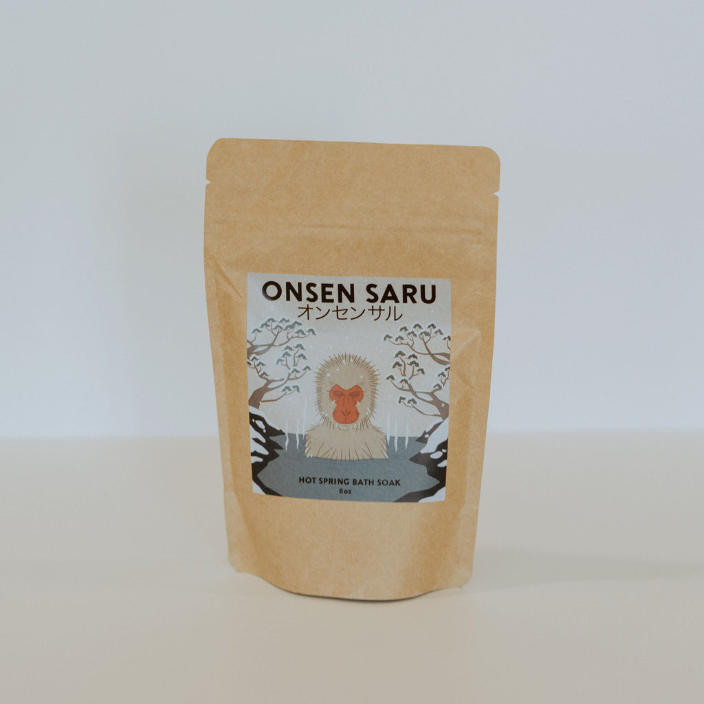 Brown paper bag with a blue label and black text reading "Onsen Saru hot spring bath soak."